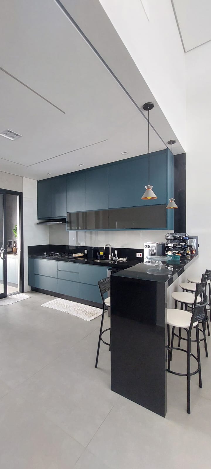 Cozinha azul-petróleo com bancada preta, banquetas e pendentes decorativos