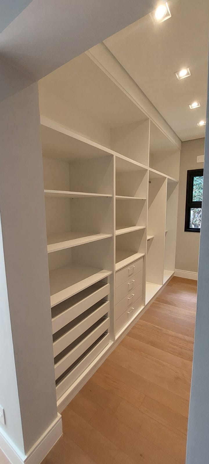 Closet branco com prateleiras e gaveteiros, janela preta