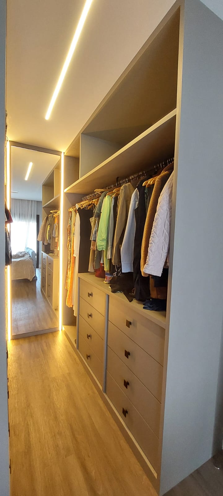 Closet greige iluminado com espelho refletindo o quarto