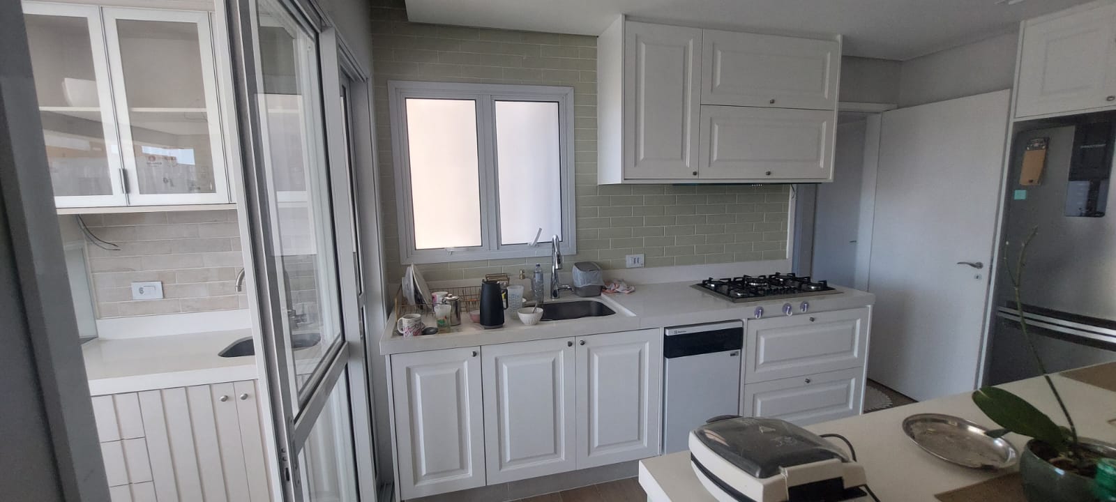Cozinha branca provençal com portas almofadadas e revestimento verde claro, objetos na pia