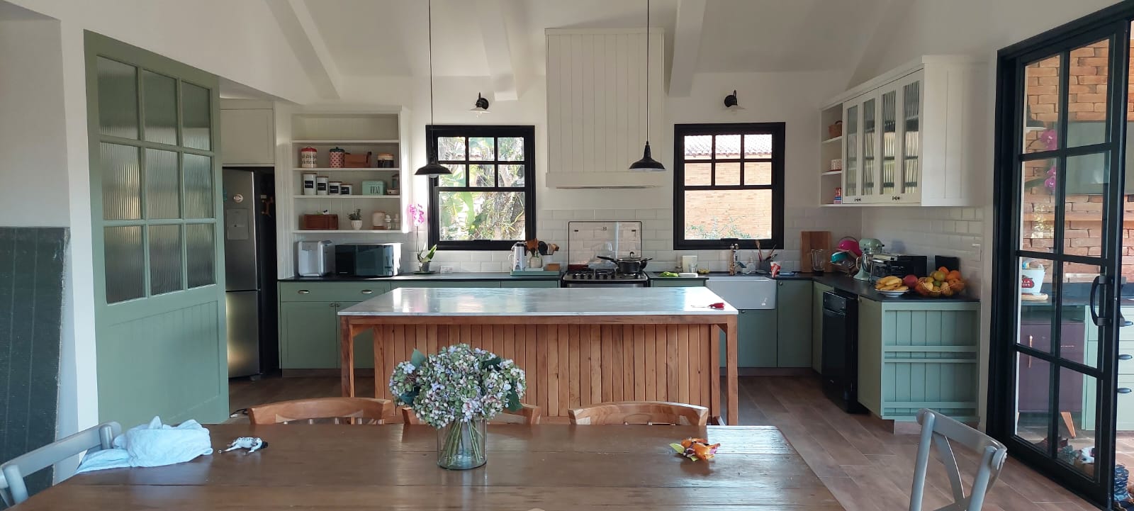 Cozinha estilo campo com armários verde-sálvia, ilha de madeira e esquadrias pretas