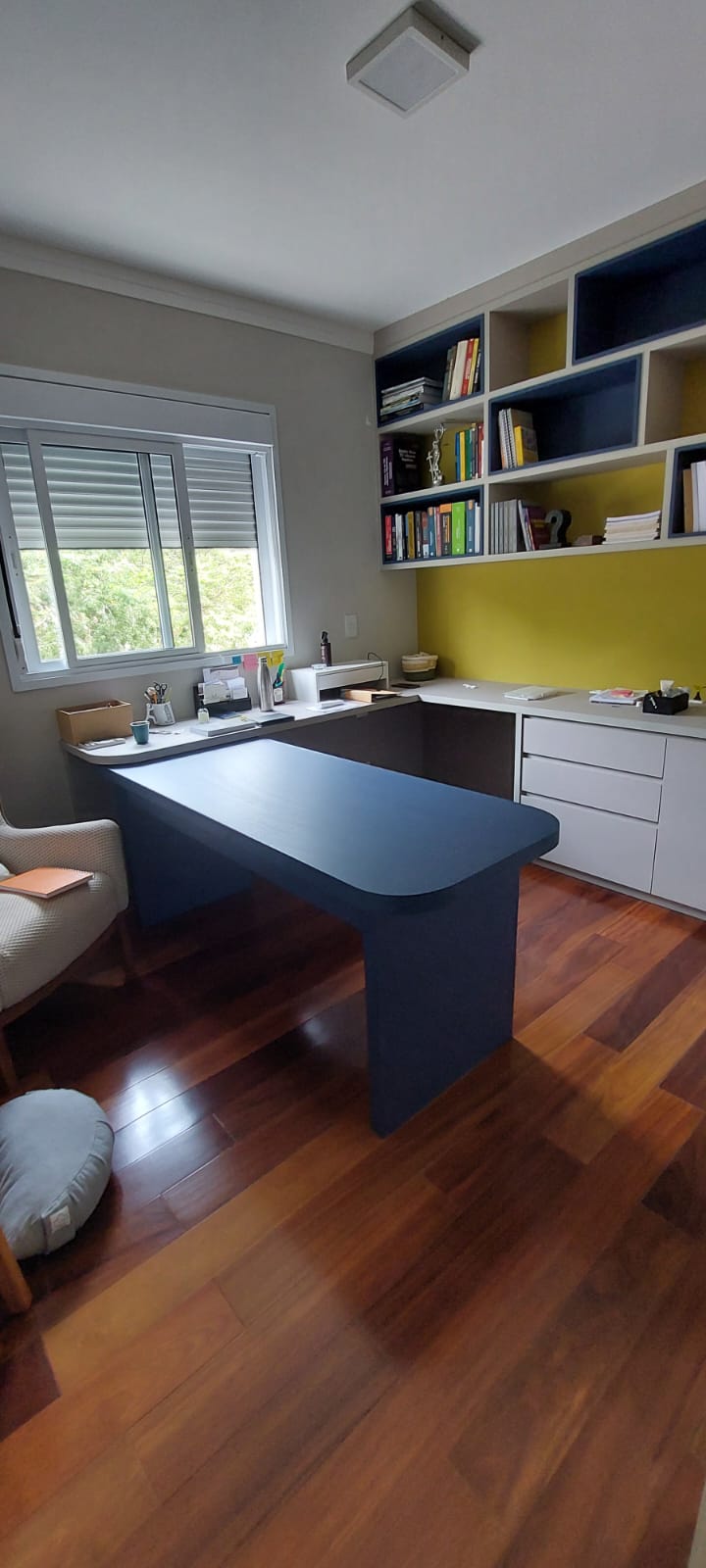 Home office com mesa azul, nichos azul-marinho e parede amarela