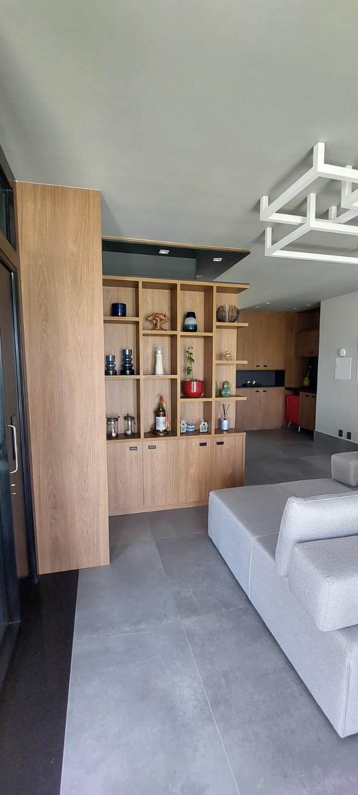 Estante de madeira com nichos decorados e sofá cinza em living integrado