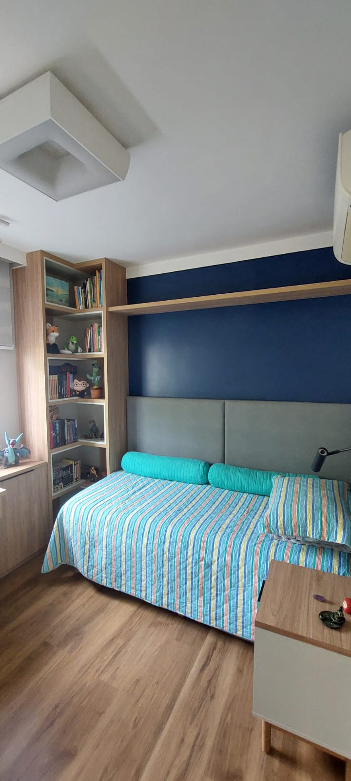 Quarto juvenil com parede azul, estante de madeira e cama turquesa