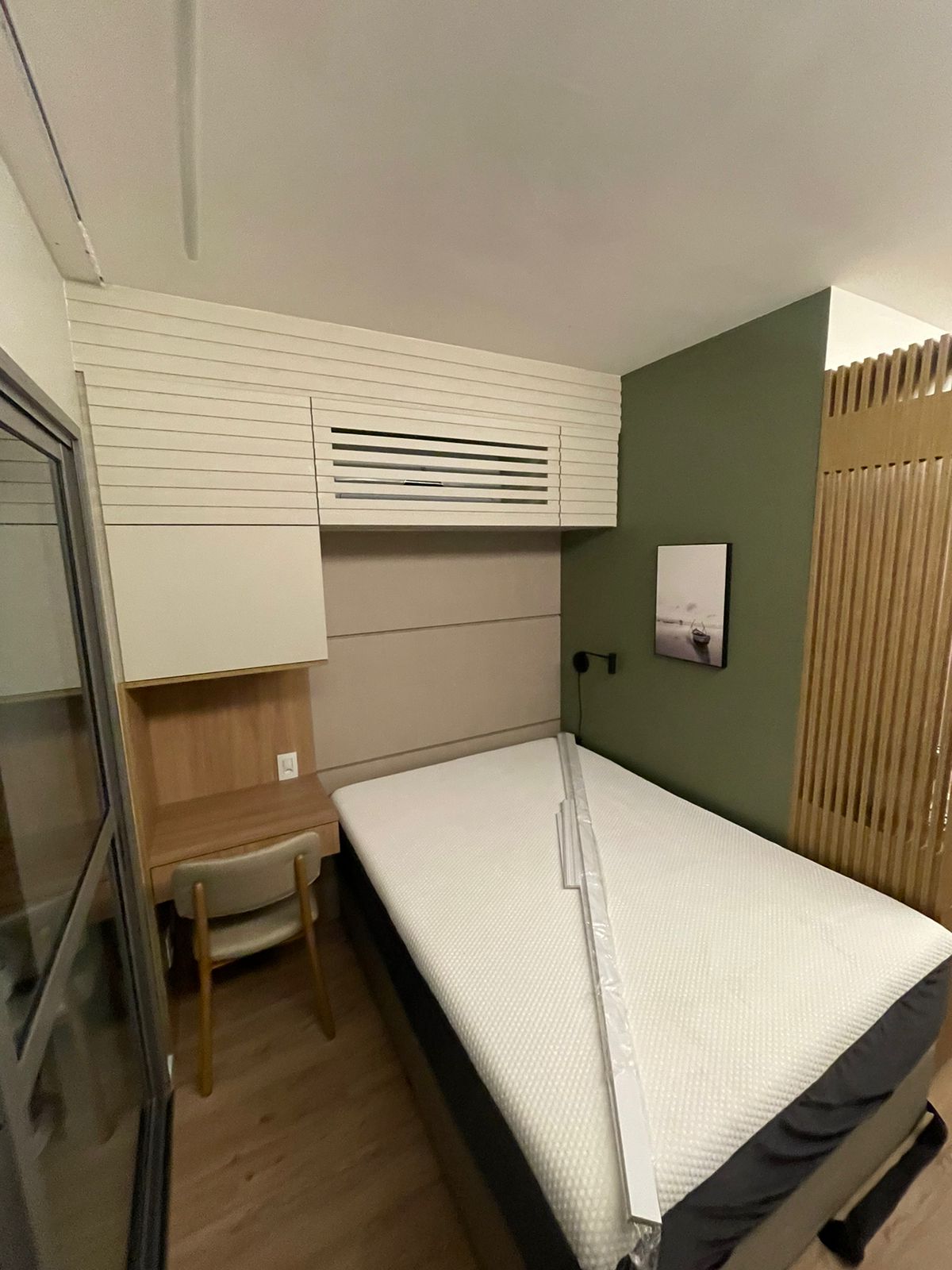 Quarto com parede verde, cabeceira estofada, escrivaninha e armário ripado