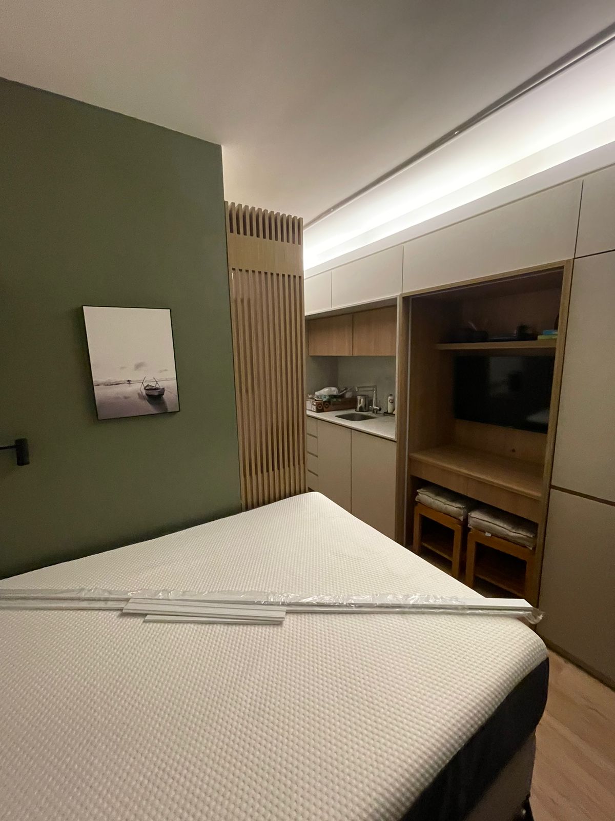 Quarto verde com colchão plastificado, kitchenette e painel de TV ao fundo