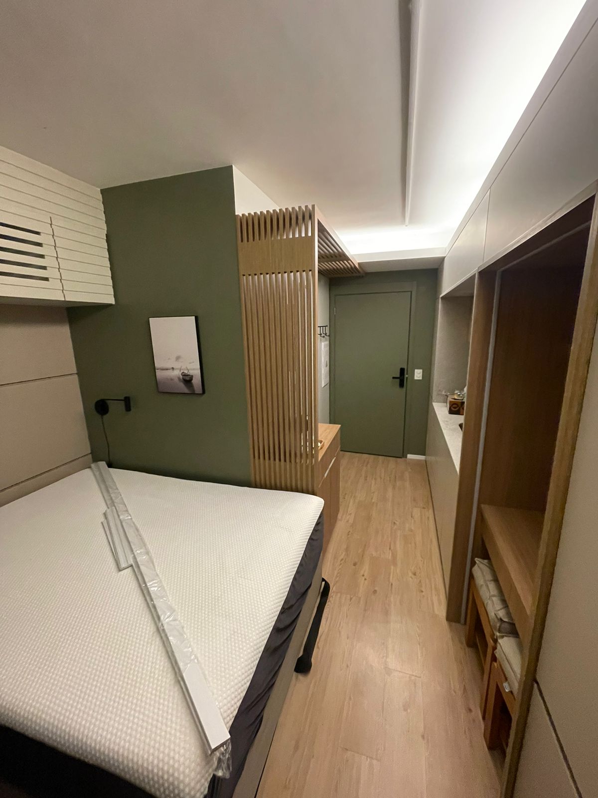 Quarto studio com parede verde, painel ripado e colchão ainda plastificado