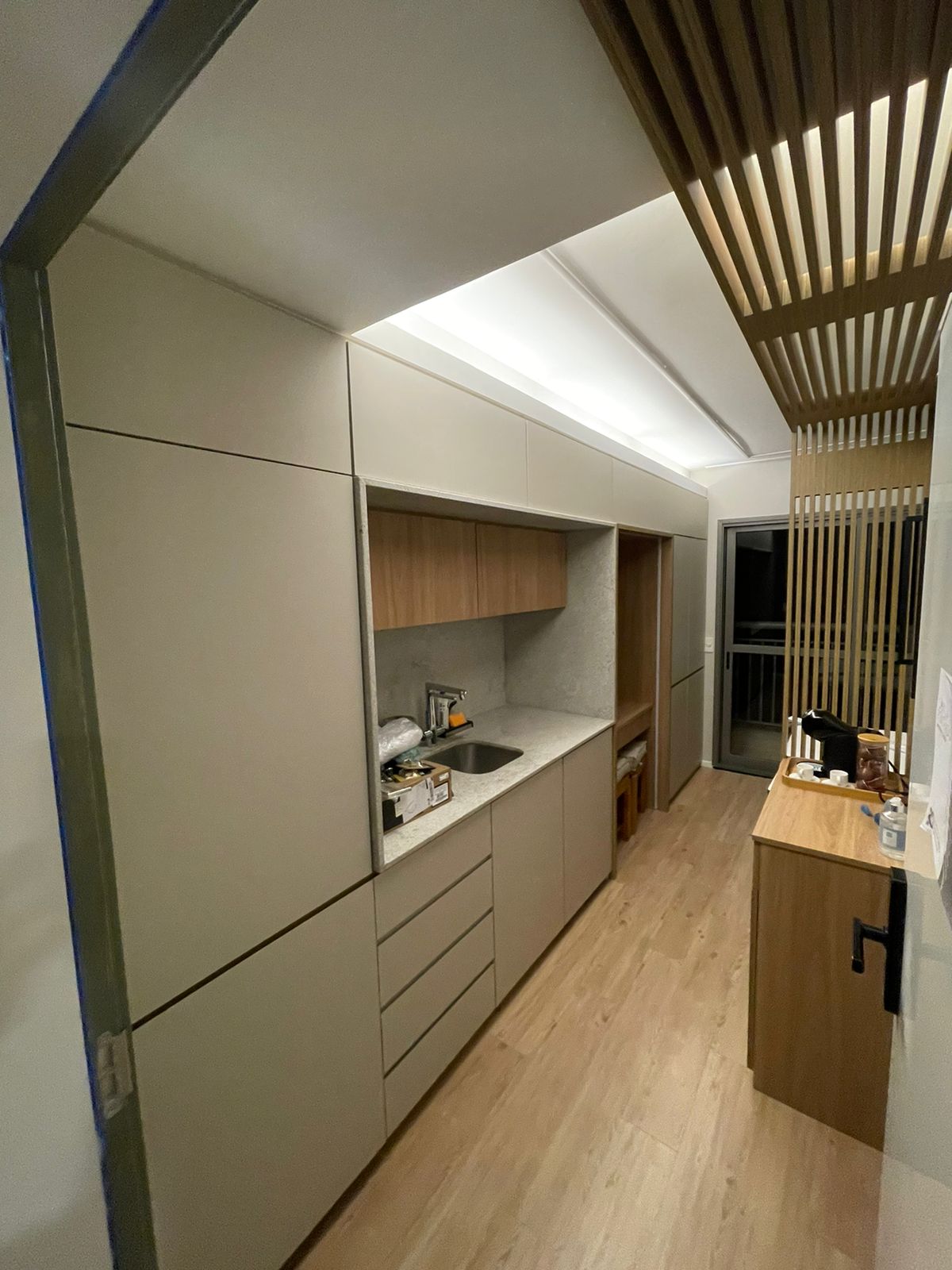 Kitchenette bege com cuba, forro iluminado e ripado de madeira