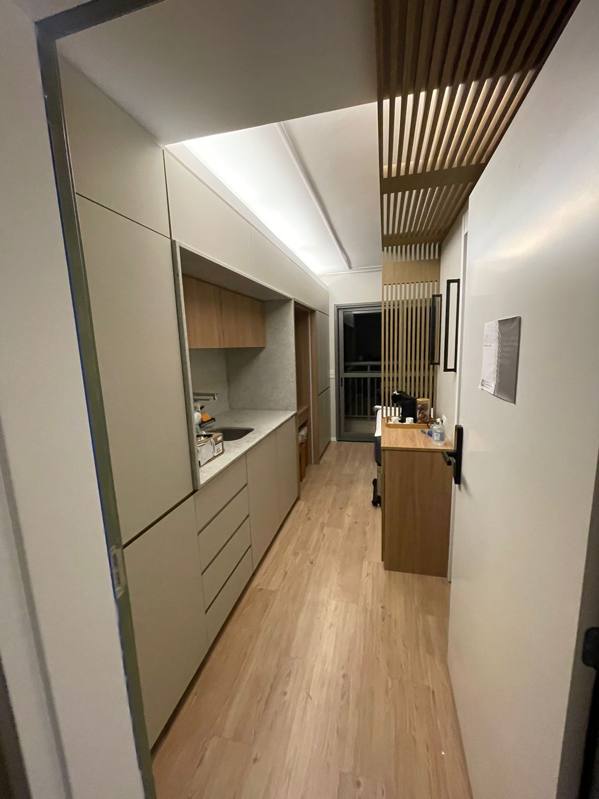 Corredor do studio com kitchenette bege e forro ripado iluminado