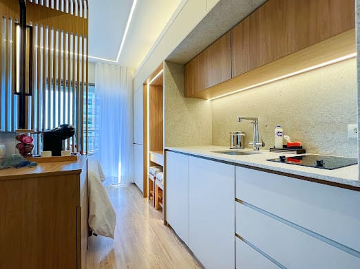 Kitchenette branca com cooktop, armários de madeira e LED sob nicho