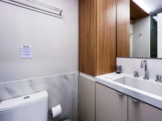 Lavabo com armário de madeira sobre bancada branca e espelho