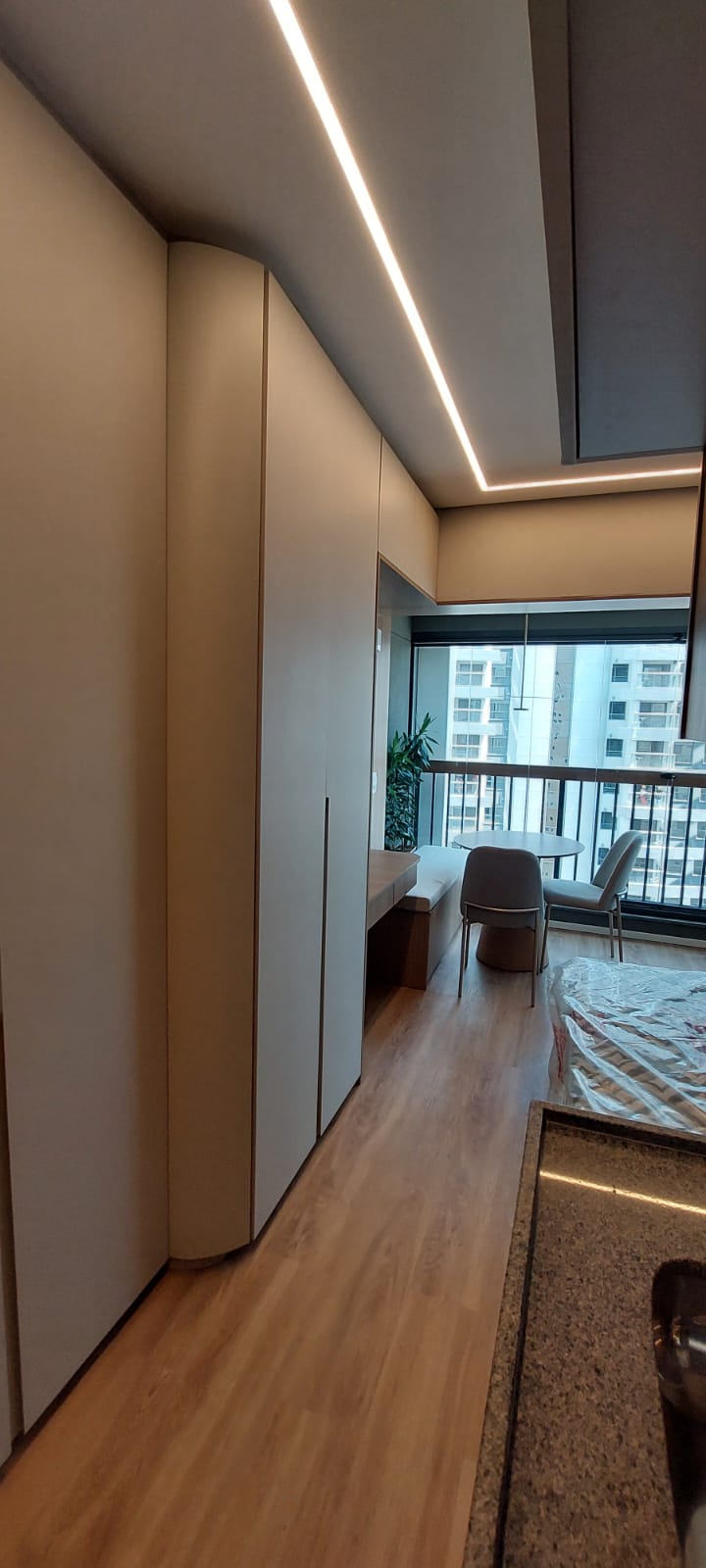 Studio com armários bege curvos, iluminação em LED e varanda com mesa