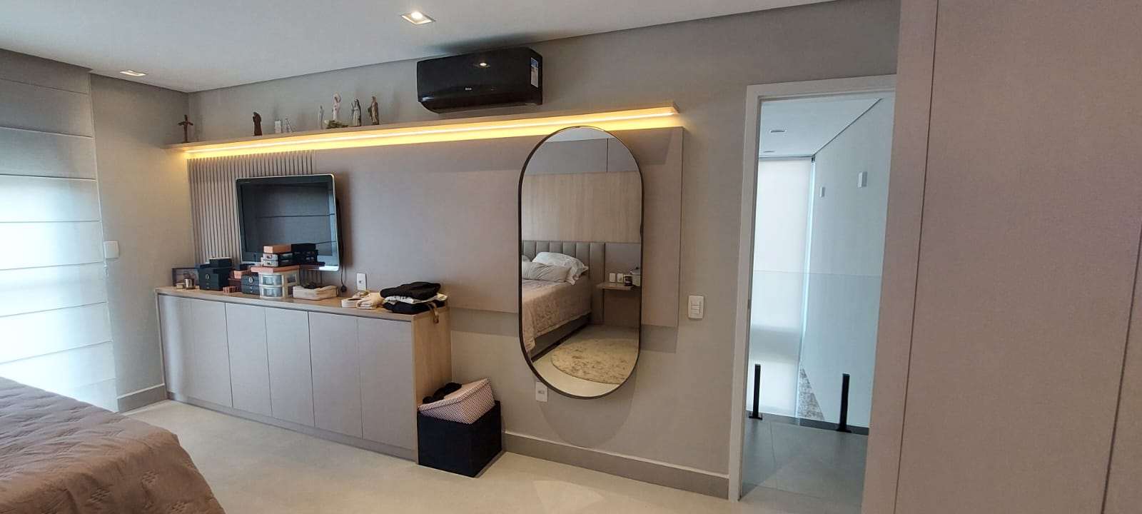 Parede de TV com prateleira iluminada e espelho oval